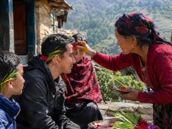 Elderly person applying Dashain Tika and jamara on a younger family member's forehead during Dashain festival in Nepal